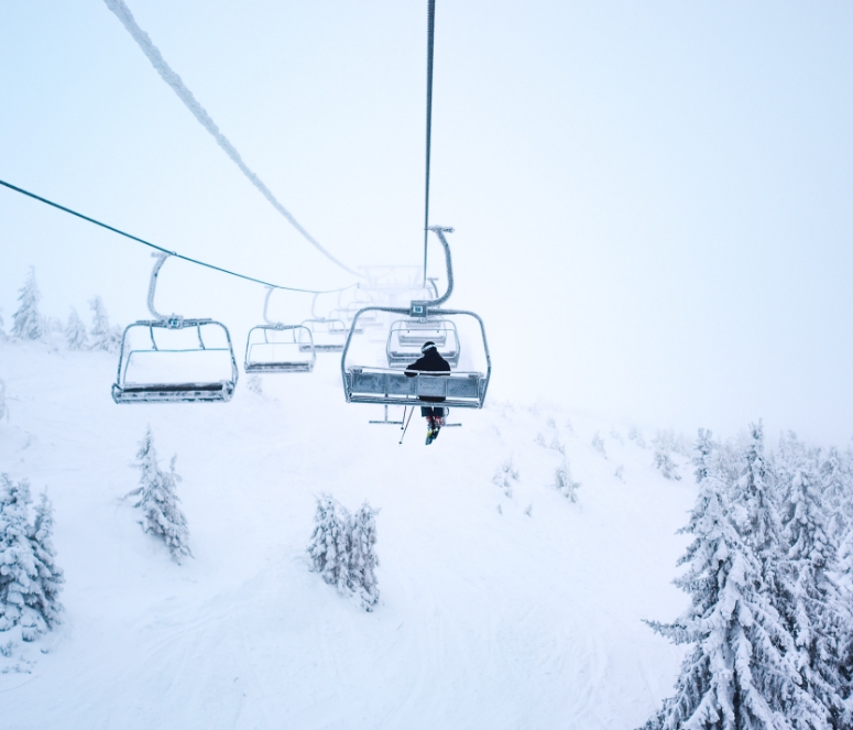 Image features someone riding on a ski lift in the snow.